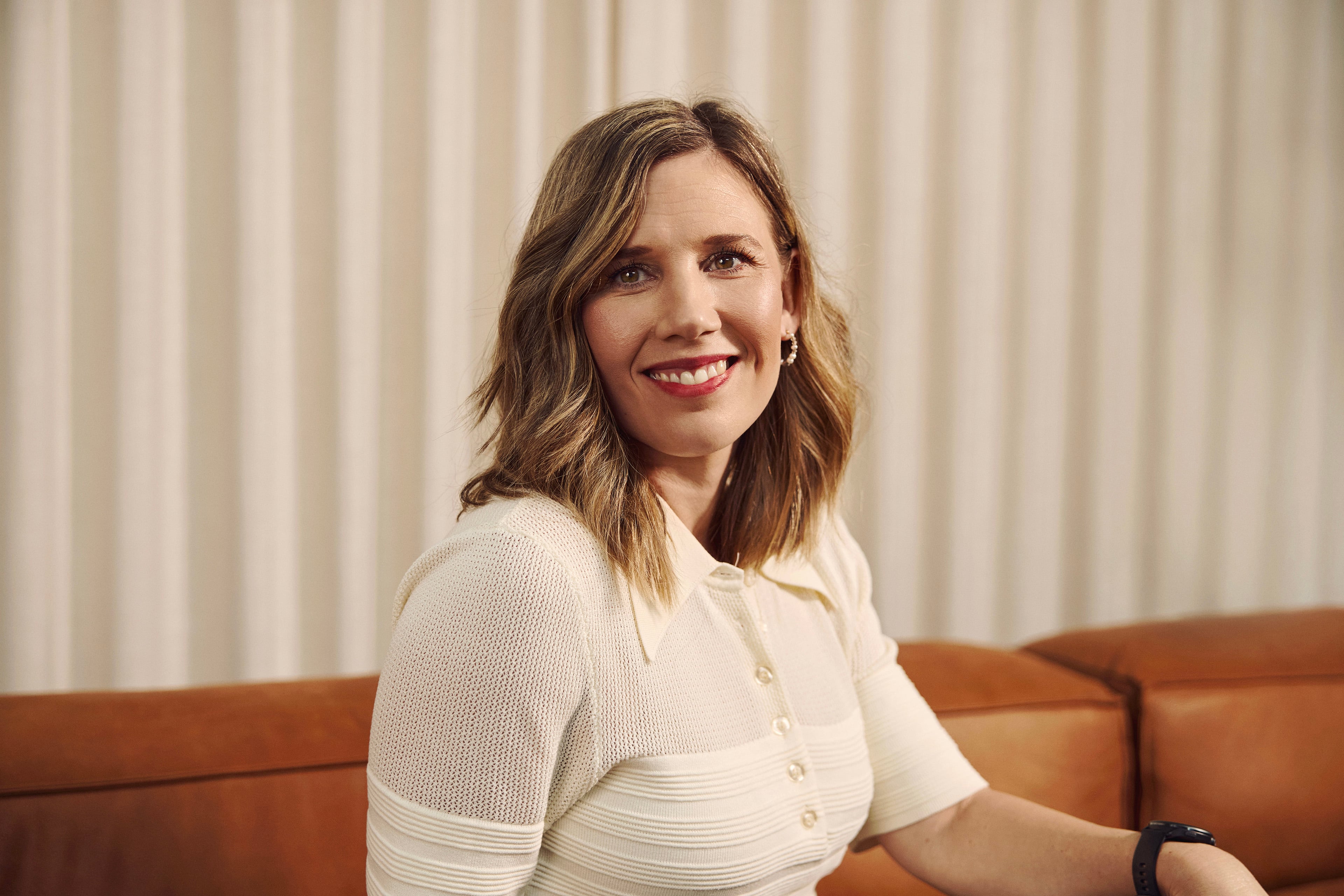 Kvinde i hvid bluse sidder på brun sofa foran lysegrå gardin